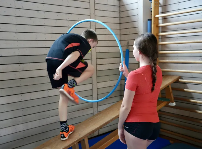 Ein Junge steigt auf der Langbank durch einen Reifen.