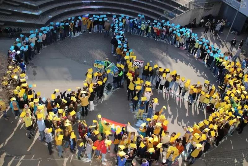 Schulgemeinschaft versammelt sich zum Peace Zeichen in Blau Gelb